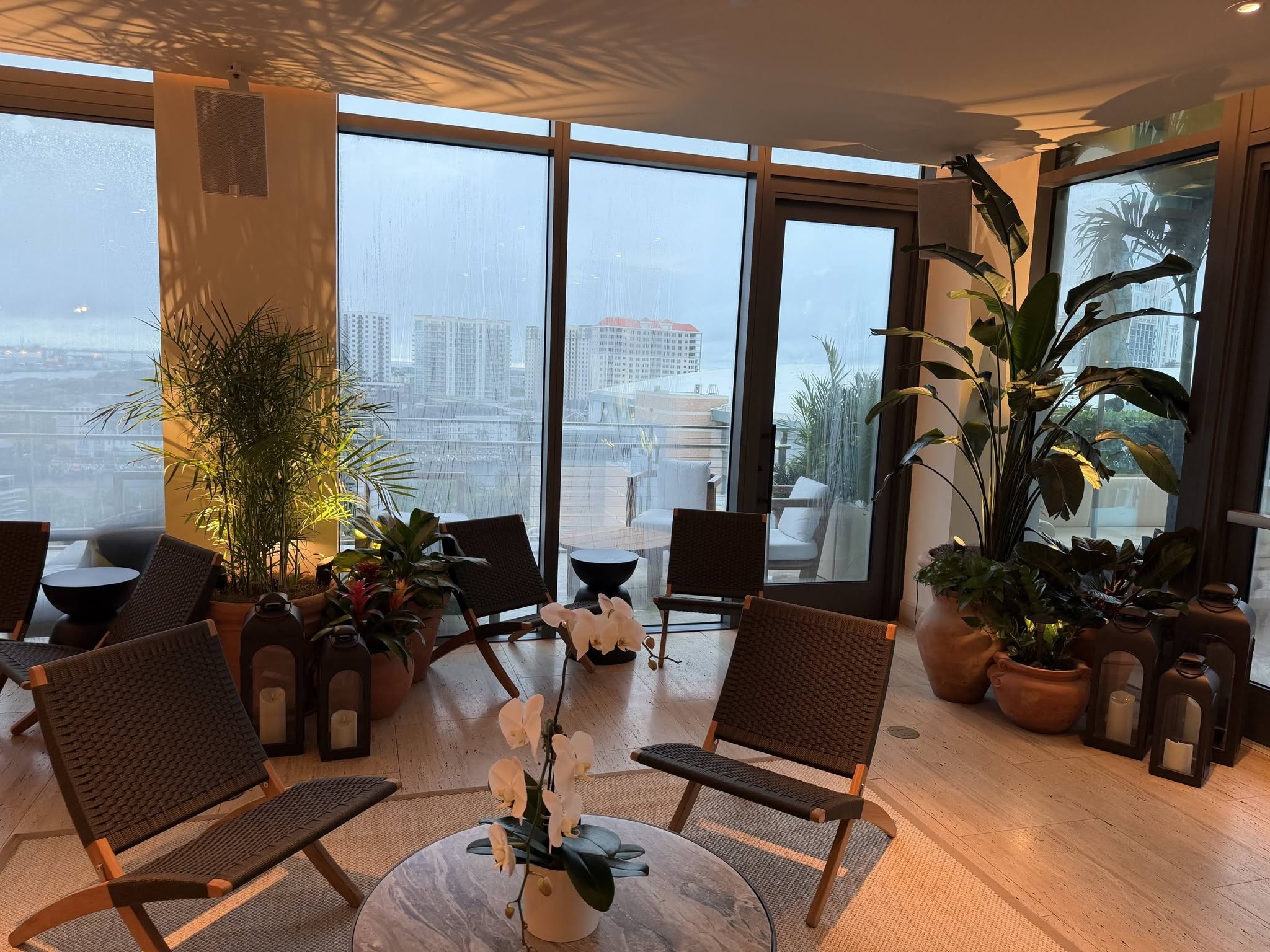 Hotel lounge with woven chairs, white orchid centerpiece, palms, and bird of paradise beside floor-to-ceiling windows