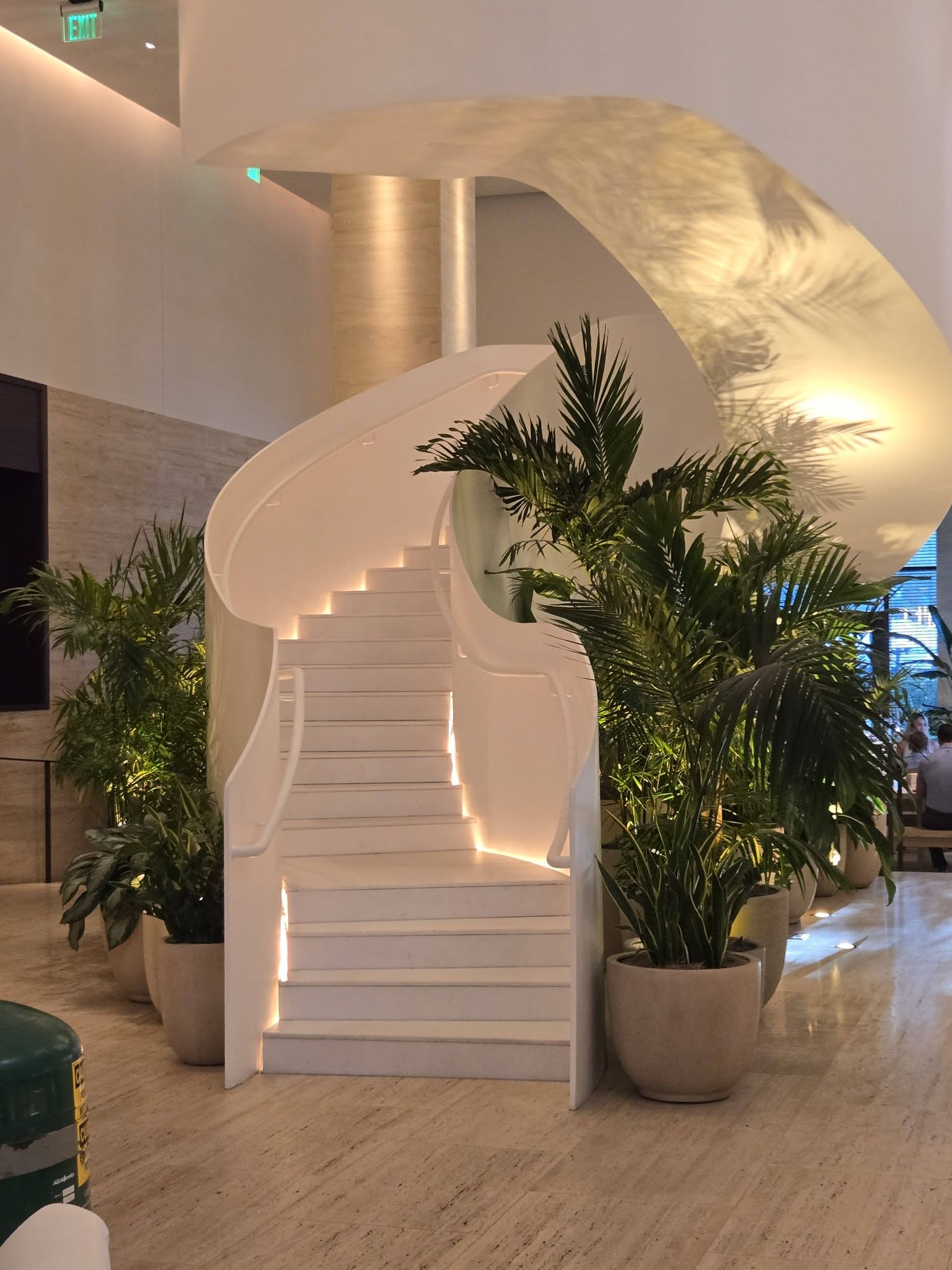 Areca palms in stone planters framing a sculptural white staircase in a hotel lobby